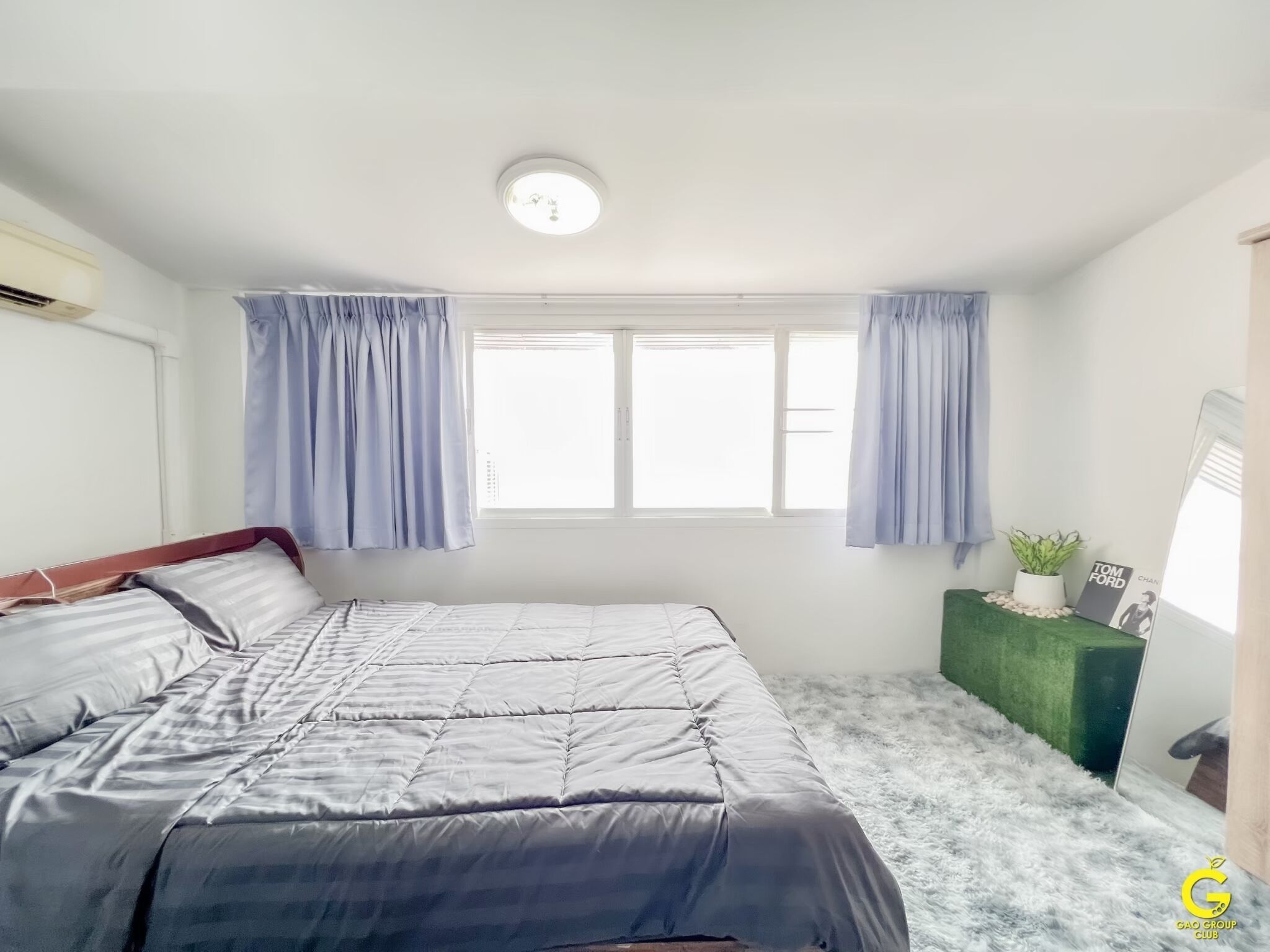 A bedroom with a bed, a window with curtains, a small plant, and a picture frame on a green side table.