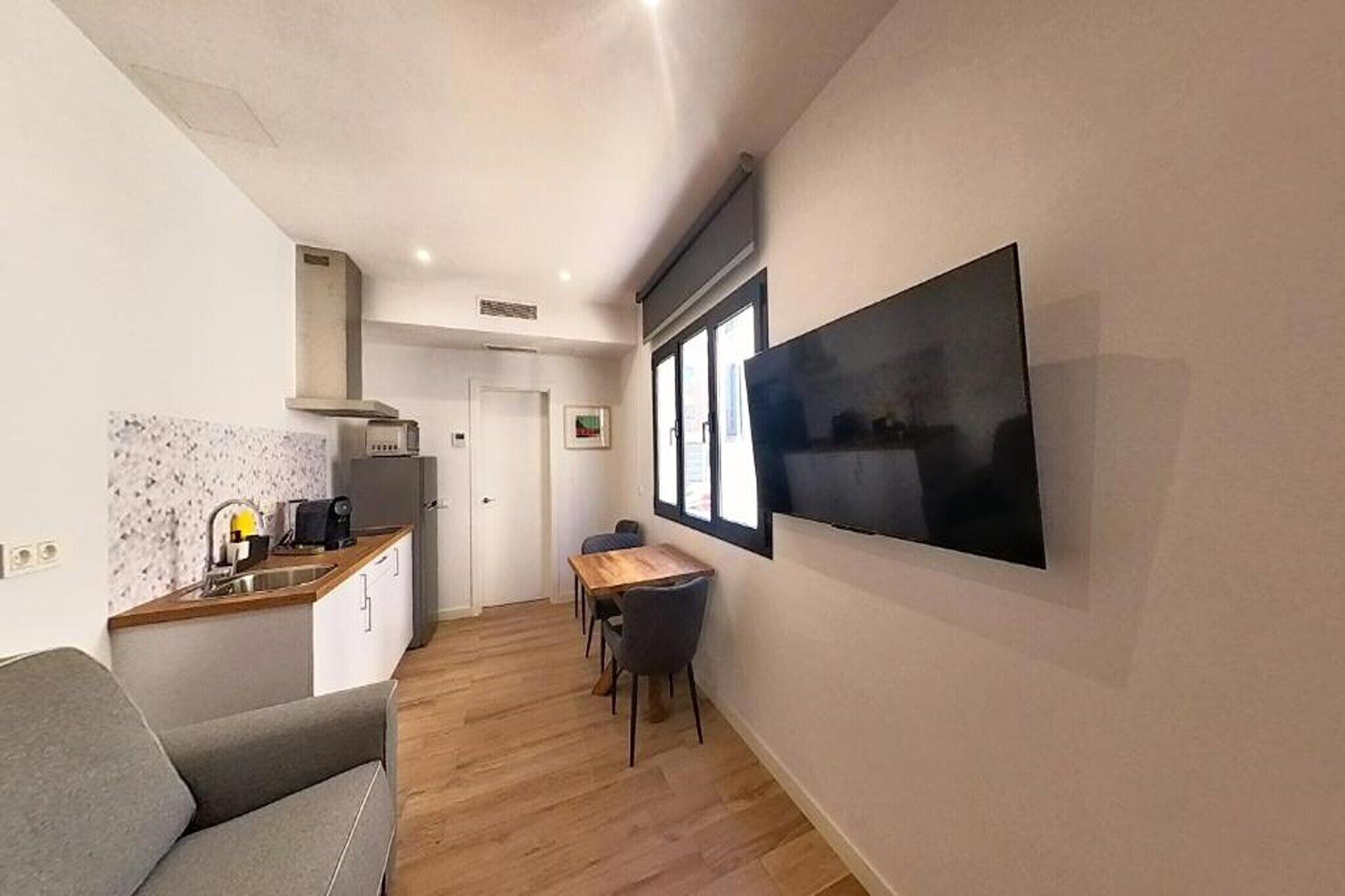 A compact living space with a kitchenette, a dining area, and a large TV mounted on the wall.