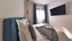 A bedroom with a bed, a hanging light, a TV on the wall, and a window with curtains.