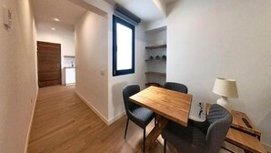 A modern, well-lit room with a wooden dining table, two chairs, and a small side table with a lamp.