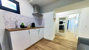A compact kitchen with white cabinets, a wooden countertop, and a backsplash. A dining area is visible in the background with a table and chairs.
