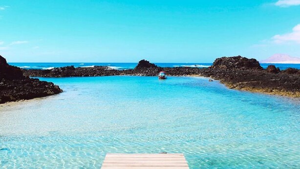 A wooden pier leading into a clear blue sea with rocky formations on either side.