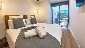 Una habitación de hotel moderna con una cama grande, un ventanal corredero al balcón y un diseño sencillo y minimalista.