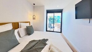 Una habitación de hotel moderna con una cama grande, un televisor montado en la pared y un ventanal corredero que da a un espacio exterior.