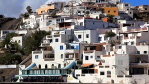 Un pueblo costero con edificios blancos, algunos con balcones, y un restaurante en la parte inferior.
