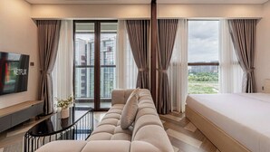 Een moderne hotelkamer met een bank, een bed, een televisie en grote ramen voorzien van gordijnen.