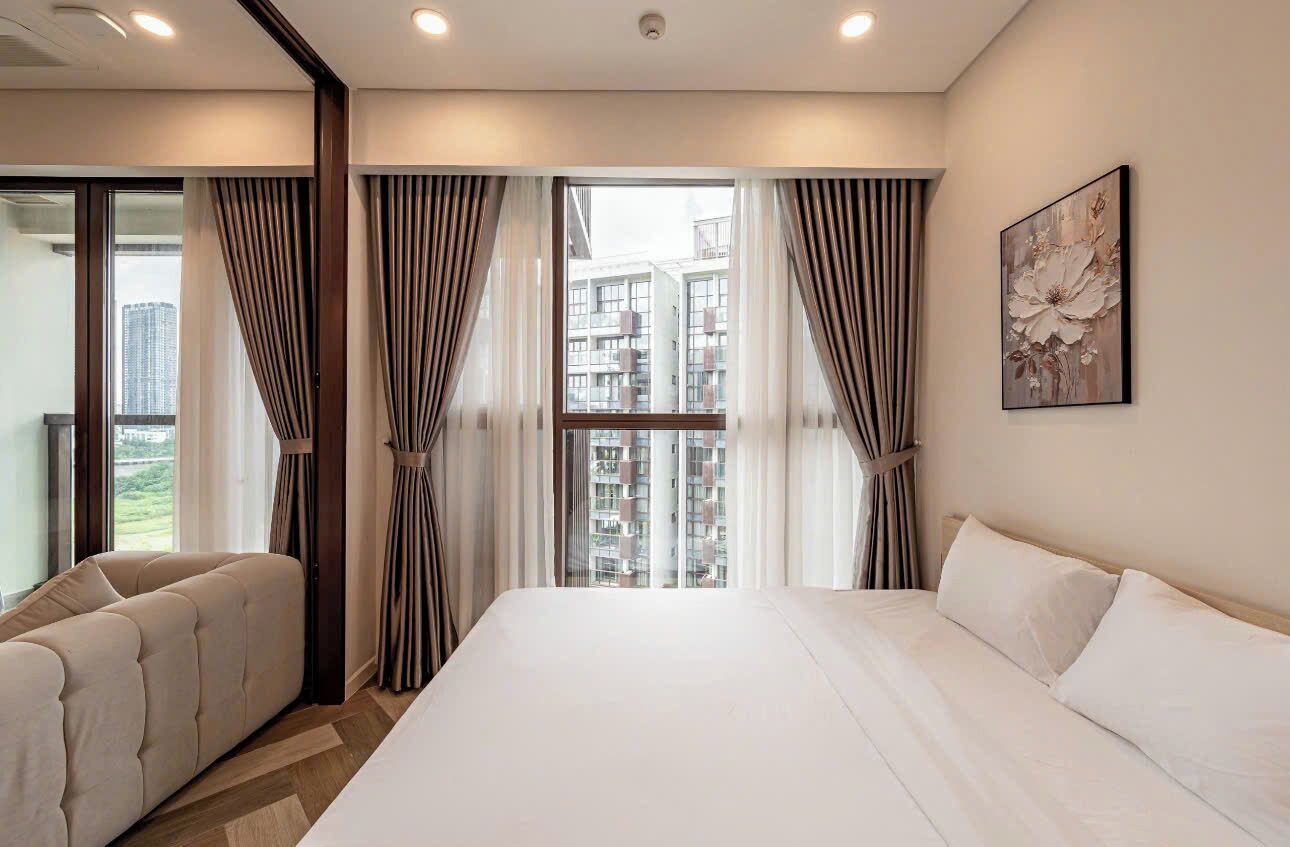 Ein Hotelzimmer mit einem großen Bett, einer Sitzecke, Blick auf Gebäude durch das Fenster und einem Gemälde an der Wand.