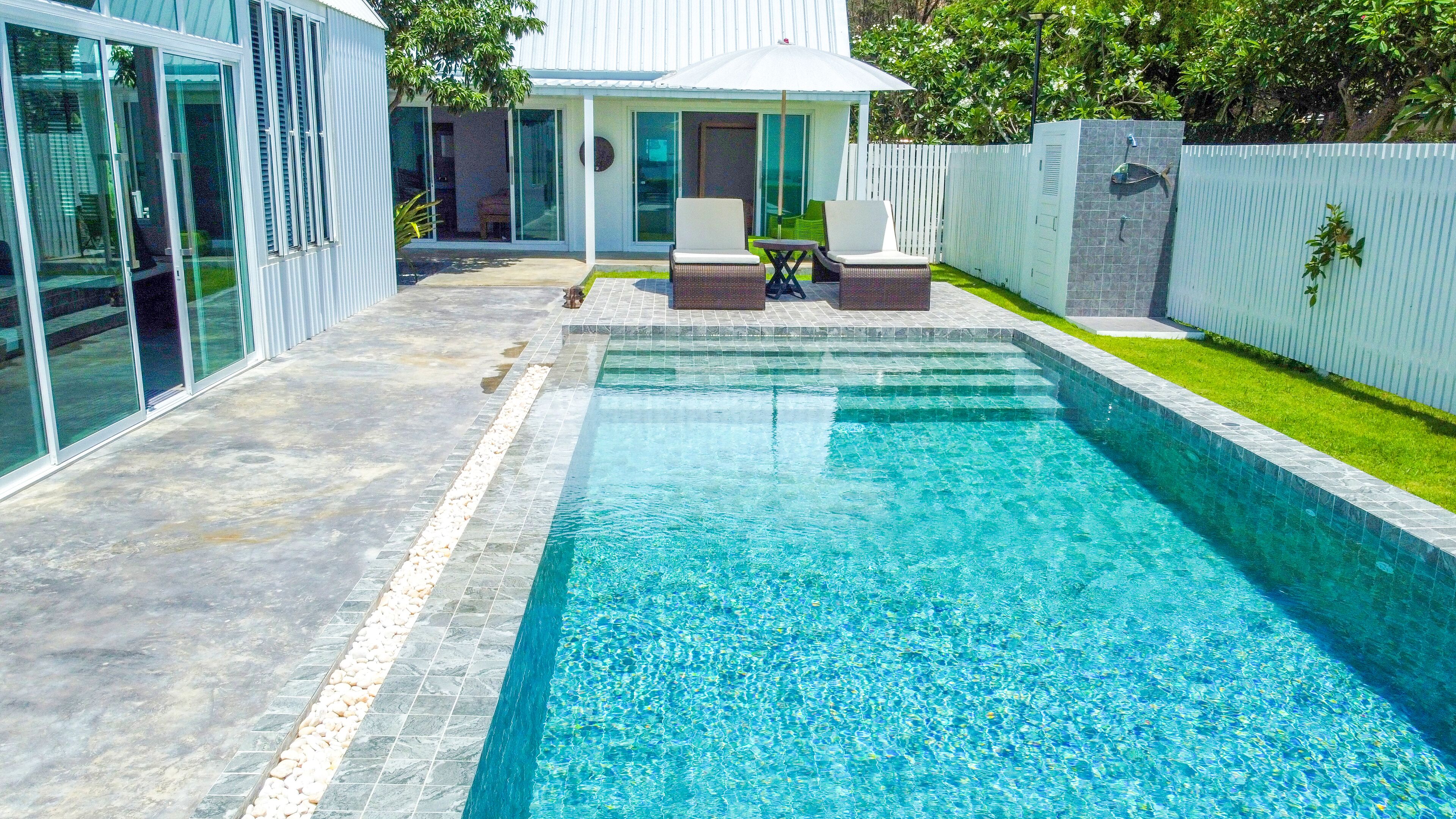 Una piscina con acqua cristallina circondata da un patio con sedie e un tavolino.