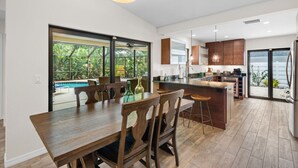 A modern kitchen with a central island, large windows, and a view of greenery.