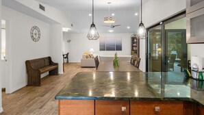 A modern kitchen with a large island, pendant lights, and a view through a glass door.