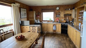 A kitchen with wooden cabinets, a dining table with chairs, a window with curtains, and a view of the outdoors.