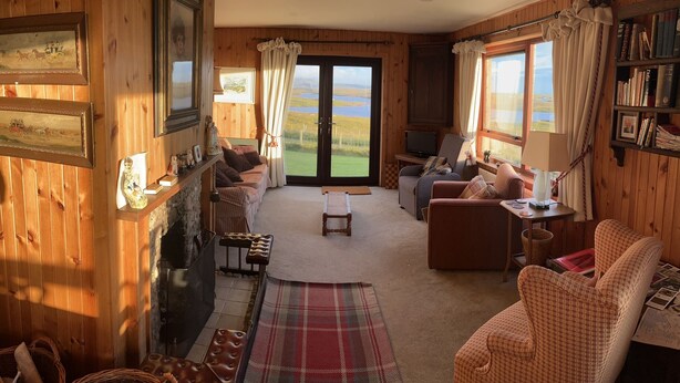A cozy room with wooden walls, a fireplace, a sofa, a coffee table, and a view of a lake through large windows.