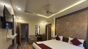 A hotel room with a large bed, a TV mounted on the wall, a desk with a chair, and a bathroom visible through an open door.