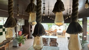 A restaurant with hanging light bulbs, wooden furniture, and a view of the outdoors.