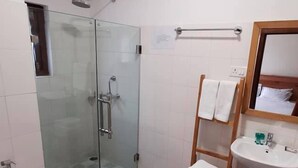 A bathroom with a glass-enclosed shower, a white sink, and a wooden shelf with towels.