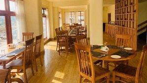 A spacious dining area with wooden tables and chairs, large windows, and a staircase leading to an upper level.
