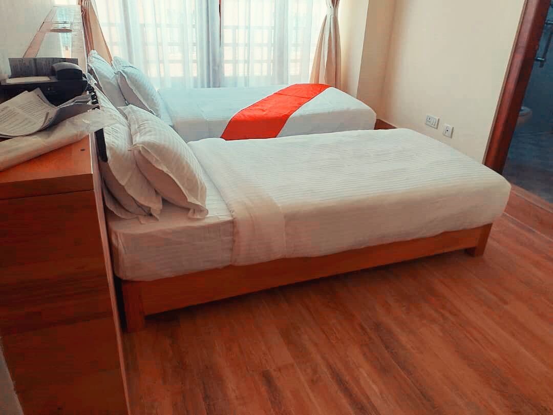 Habitación de hotel con dos camas, un escritorio de madera con lámpara y una ventana con cortinas.