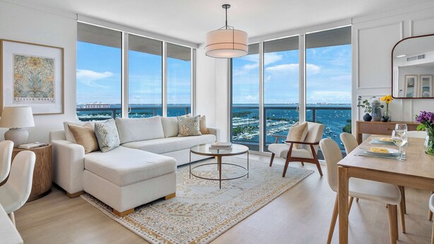 A spacious living area with a sofa, coffee table, and dining table, large windows with a view of the sea, and a modern pendant light. - Modern Residence with Pool Access | Coconut Grove (Miami)