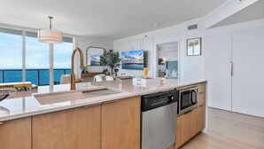 A modern kitchen with a large island, built-in appliances, and a view of the sea. - Panoramic Vistas | Modern Apartment in Coconut (Miami)