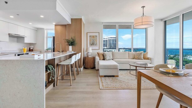 A modern apartment with a kitchen, dining area, and living room. It features a large window with a city view, a dining table, and a sofa. - Panoramic Vistas | Modern Apartment in Coconut (Miami)