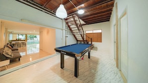 A pool table in a spacious room with a wooden ceiling, a staircase, and a view of a dining area. - GAO Phala beachfront hostel & pool villa (Ban Chang)