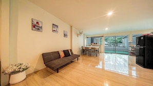 A modern living room with a sofa, dining table, and chairs, a refrigerator, and a view of the outdoors. - GAO Phala beachfront hostel & pool villa (Ban Chang)