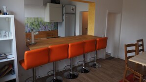 Eine moderne Küche mit einer Holzausziehtafel, vier orangefarbenen Barhocker und einem weißen Kühlschrank.