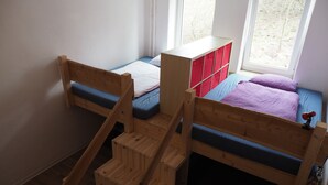 Ein Zimmer mit Etagenbetten, einer Holztreppe und einem Fenster mit Blick auf Bäume.