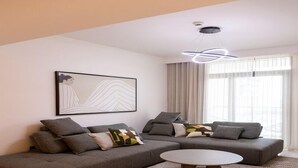 A modern living room with a sectional sofa, a round coffee table, and a contemporary light fixture. - Tranquil 1BR Haven in the Heart of Vista (Dubai)