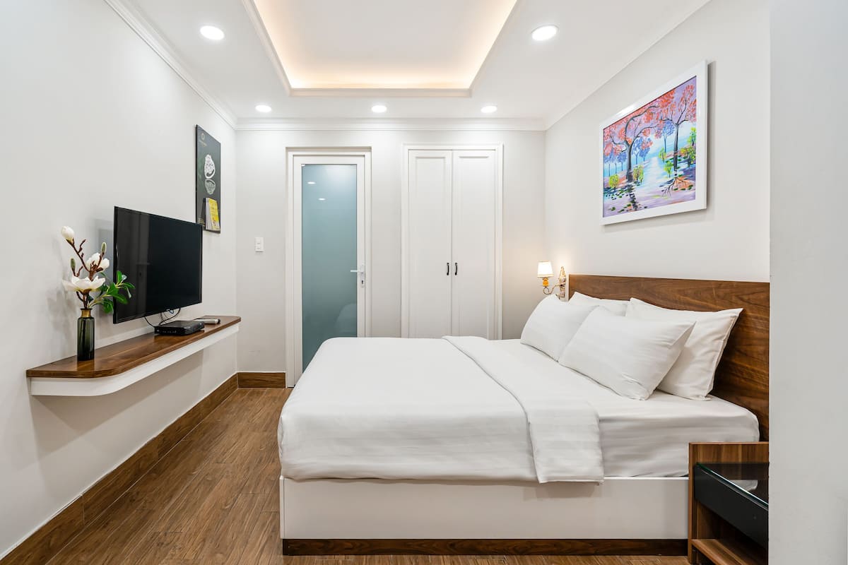 Ein modernes Hotelzimmer mit einem großen Bett, einem Flachbildfernseher, einem Nachttisch aus Holz und einem Bild an der Wand.