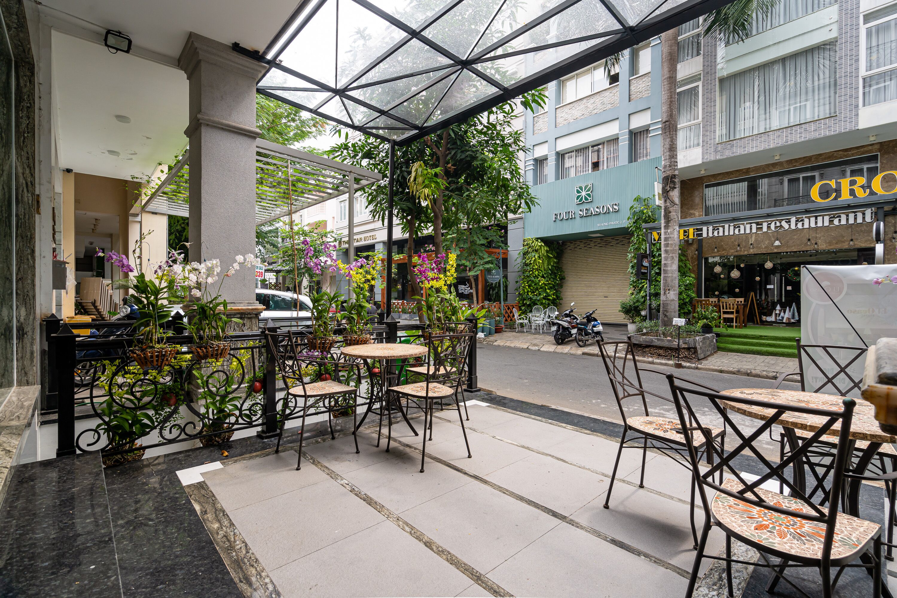 An outdoor cafe area with tables and chairs, surrounded by potted plants and flowers.