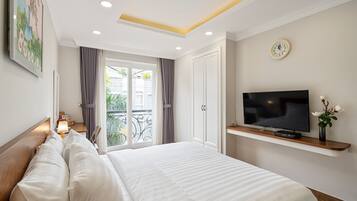 Quarto de hotel com uma cama grande, uma TV em uma estante, um relógio na parede e uma varanda com cortinas.