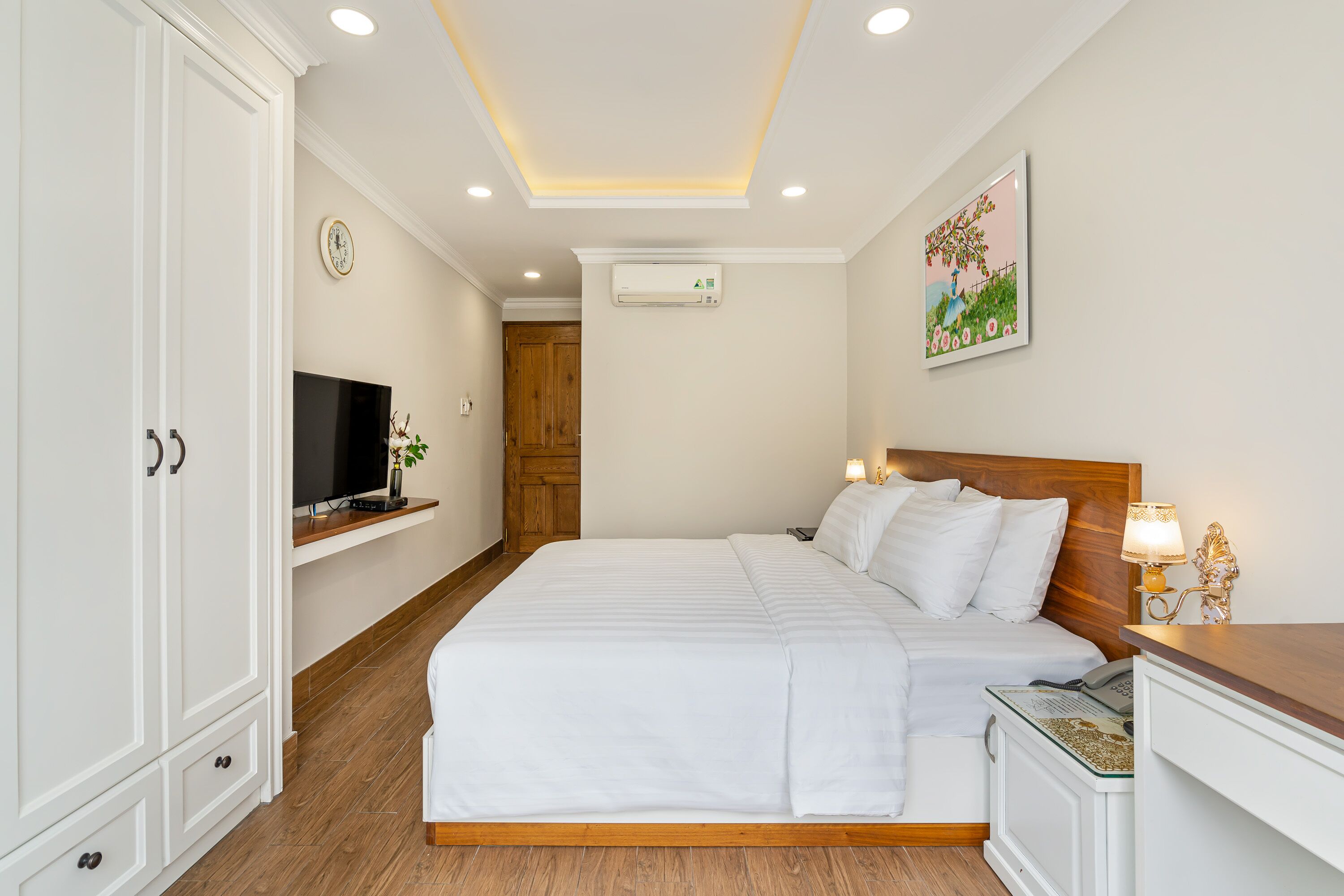 Habitación de hotel ordenada con una cama grande, un televisor en un estante de madera, un aire acondicionado de pared y un cuadro en la pared.