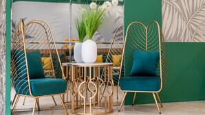 Two teal cushioned chairs with gold wireframe backs and legs, a white vase with green foliage, and a gold wire table. - El Ocaso Boutique Hotel (Ho Chi Minh City)
