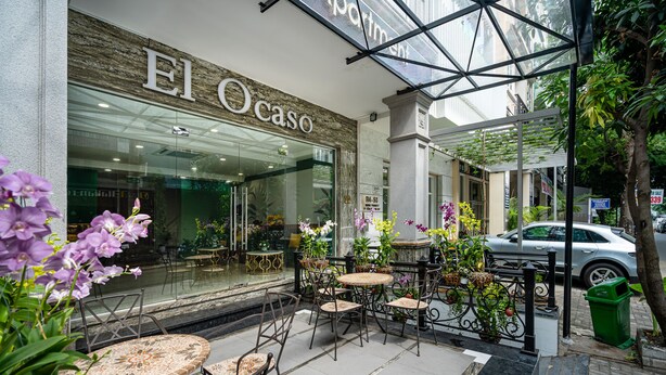An outdoor cafe area with tables and chairs, a glass storefront with the name "El Ocaso", and a car parked nearby. - El Ocaso Boutique Hotel (Ho Chi Minh City)