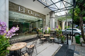 An outdoor cafe area with tables and chairs, a glass storefront with the name "El Ocaso", and a car parked nearby. - El Ocaso Boutique Hotel (Ho Chi Minh City)