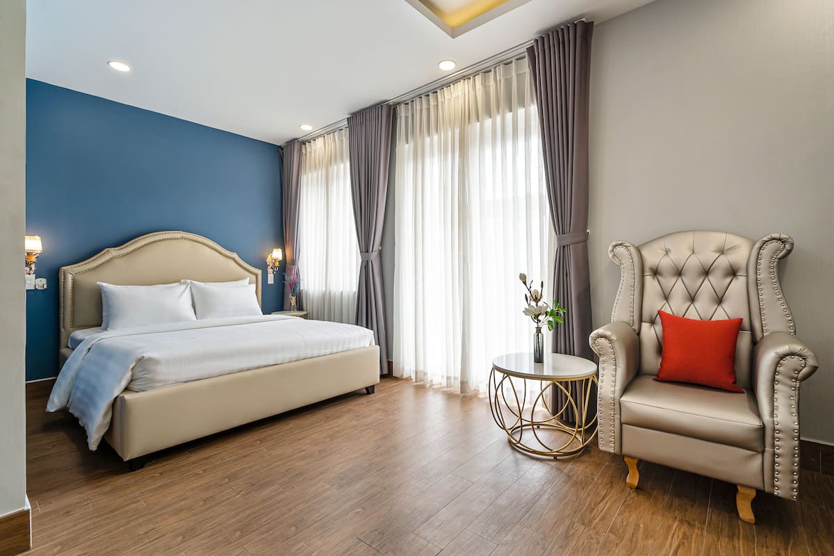 Ein Schlafzimmer mit einem Bett, einem Sessel, einem kleinen Tisch und Vorhängen.