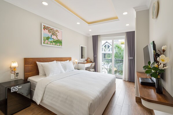 A hotel room with a large bed, a desk, a TV, and a balcony with a view of greenery. - El Ocaso Boutique Hotel (Ho Chi Minh City)