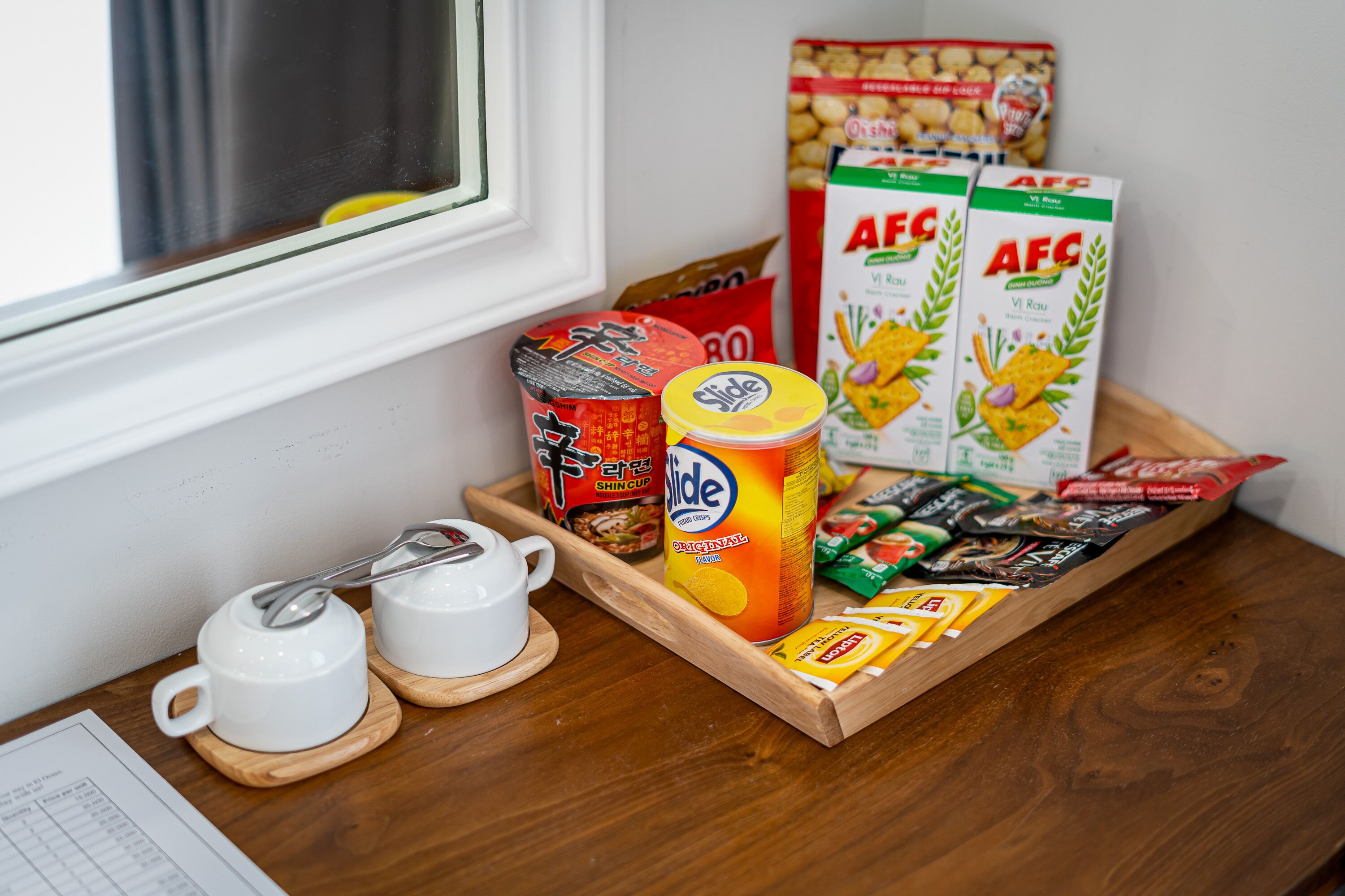 A wooden tray with food items and a can of Slide, a box of AFG cereal, and a packet of snacks on a table.