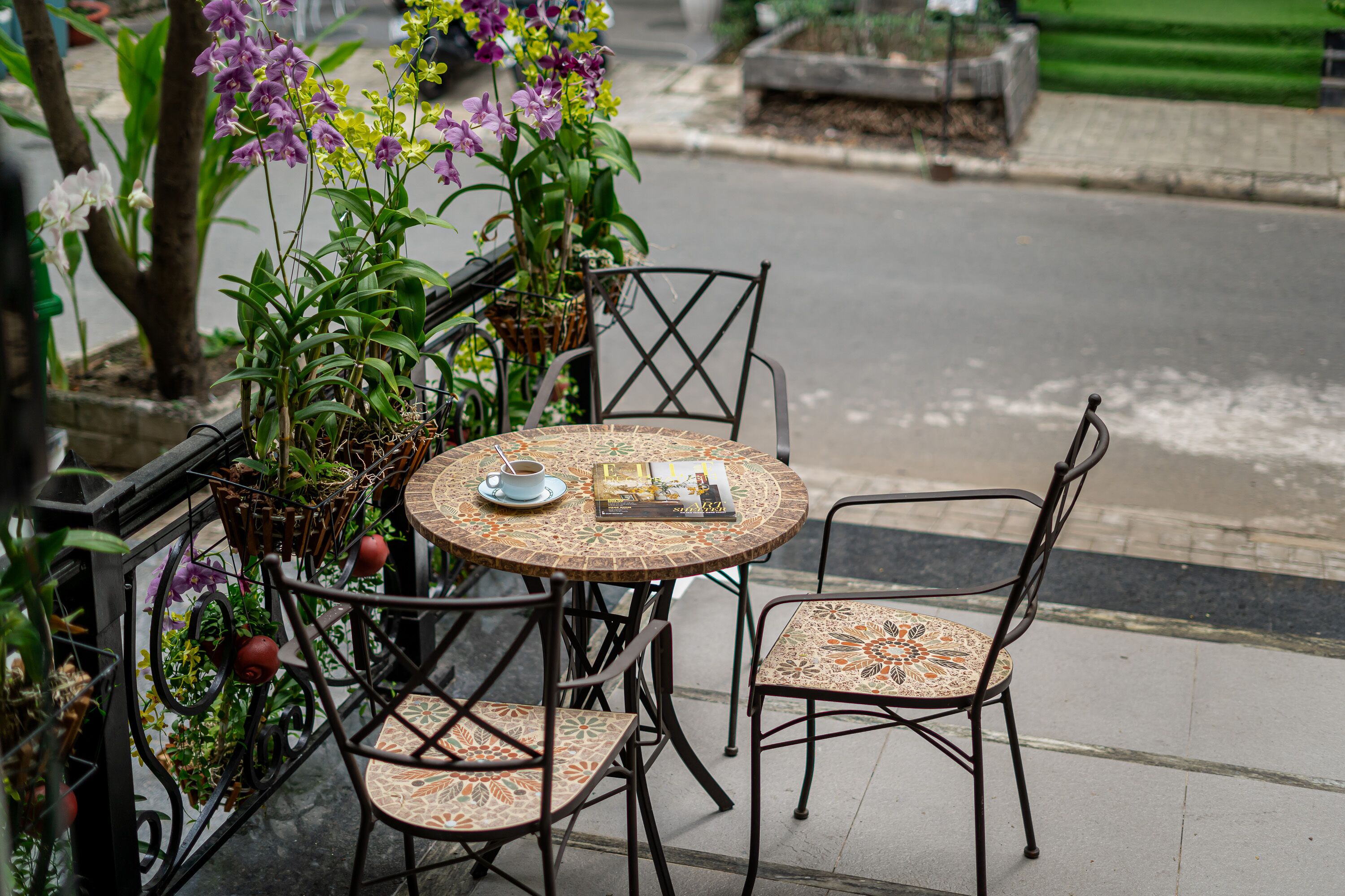 A round outdoor table with four chairs, surrounded by potted plants and flowers.