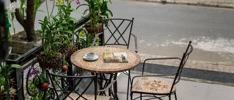 A round outdoor table with four chairs, surrounded by potted plants and flowers.