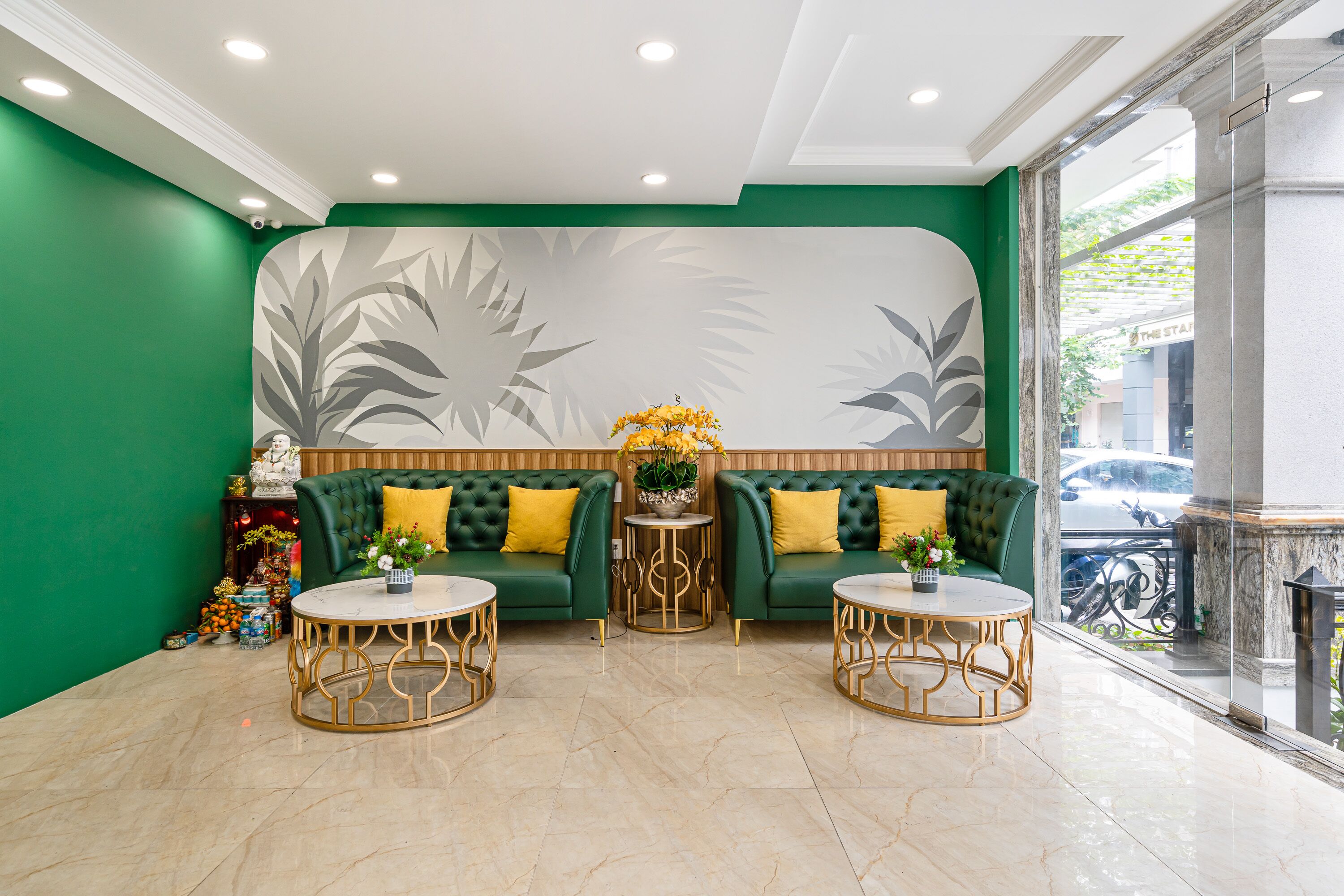 A green-walled lobby with two green sofas, gold-framed coffee tables, and a decorative wall with leaf patterns.