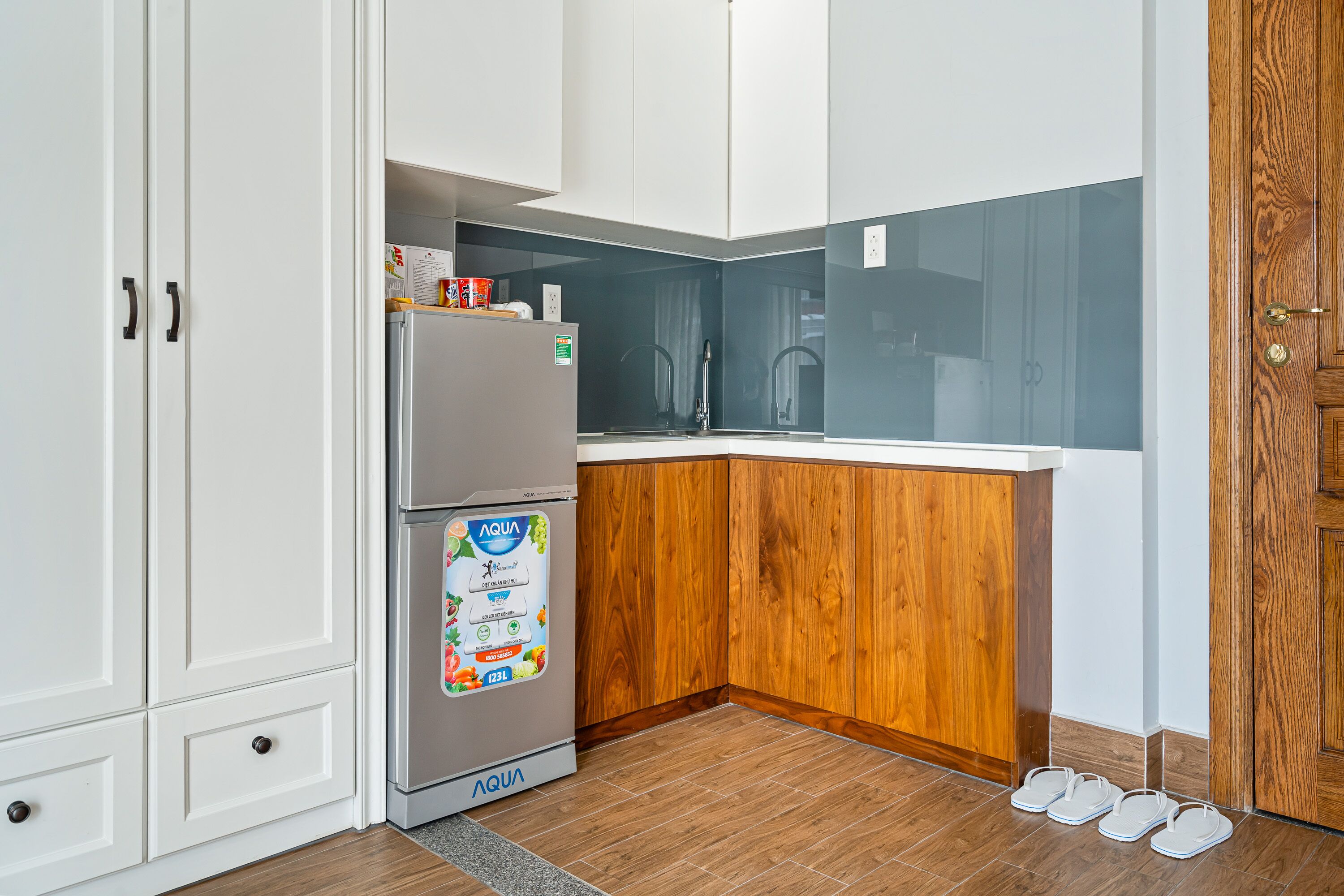A kitchen with white cabinets, a wooden countertop, a stainless steel refrigerator, and a pair of shoes on the floor.