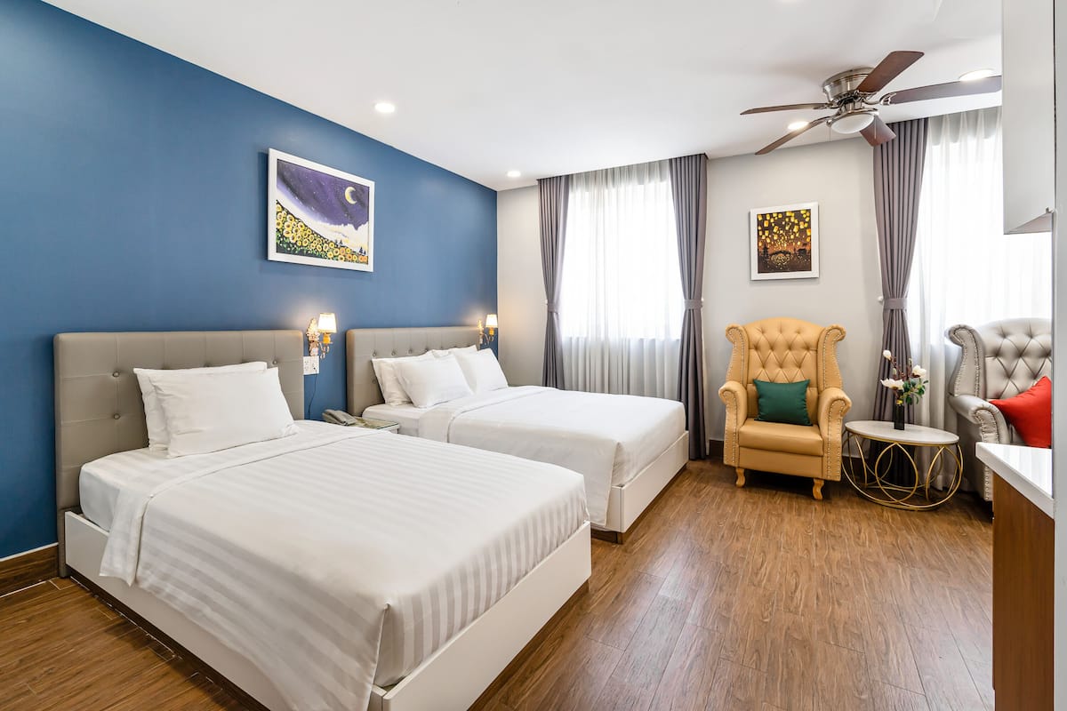 Ein Hotelzimmer mit zwei Betten, einem Deckenventilator und einer Sitzecke mit Stuhl und Tisch.