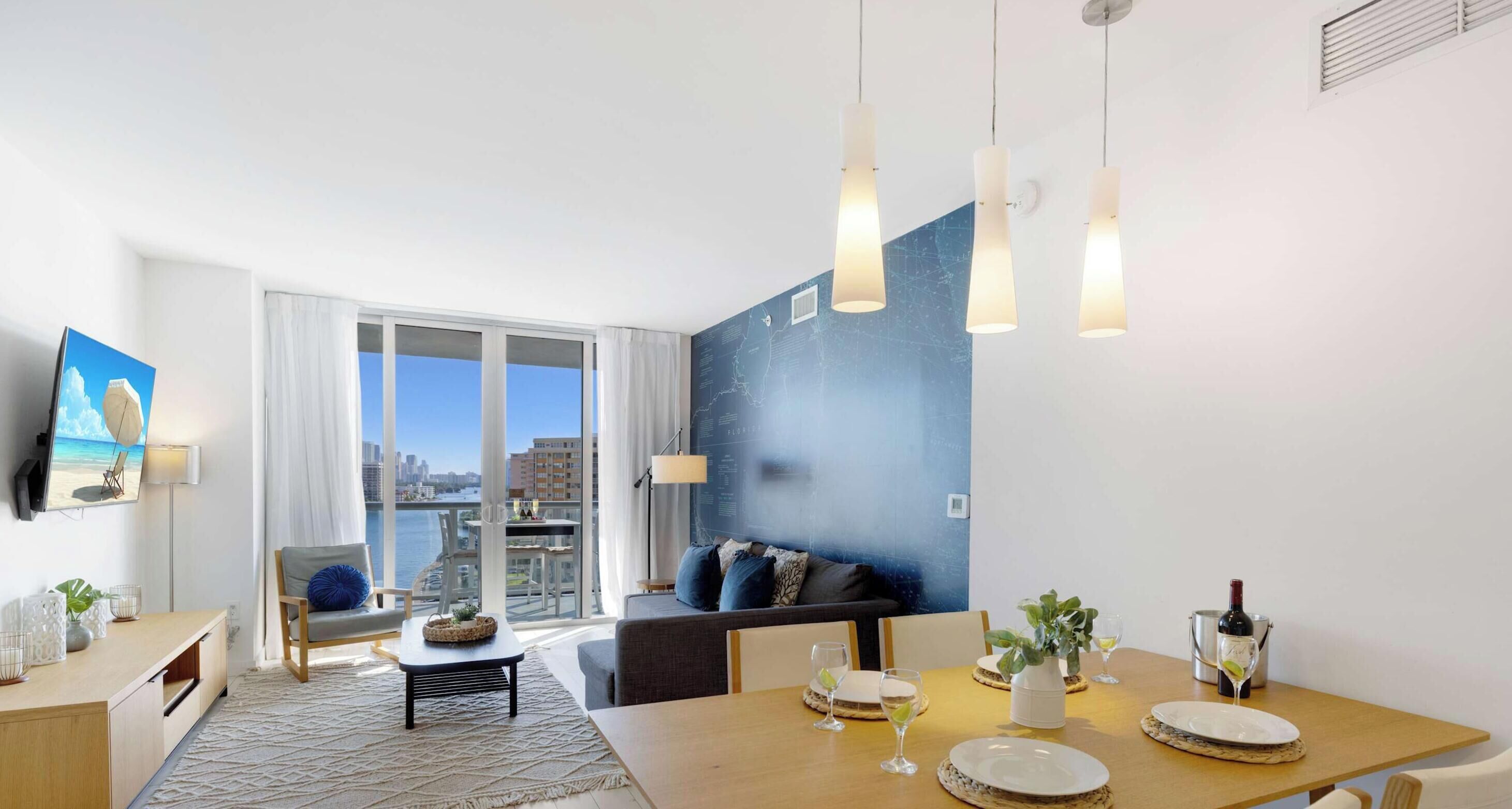 Ein modernes Wohnzimmer mit großem Fenster, einem Essbereich mit Tisch für zwei Personen und einer gemütlichen Sitzecke mit Sofa.