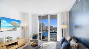 Una habitación de hotel moderna con vistas a la ciudad, un balcón con vista al agua y un cuadro grande de una playa.