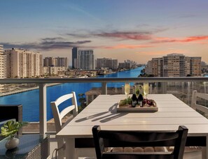 Un balcón con una mesa para dos, con vista a un paisaje urbano y un río.