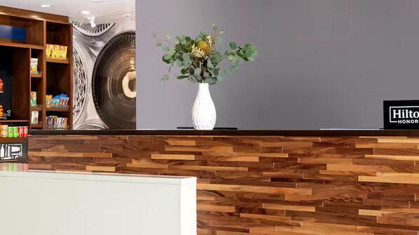 A reception area with a wooden reception desk, a white vase with green foliage, and a wall with a circular design.