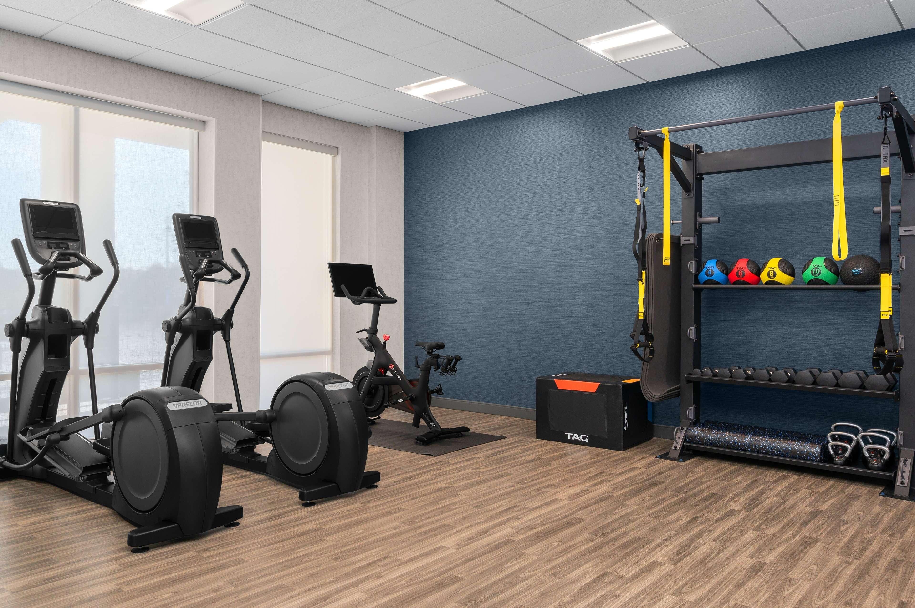Une salle de sport équipée de tapis de course, d’un vélo elliptique, d’un vélo d’appartement, d’un support à squats avec des poids et d’un tapis de yoga.