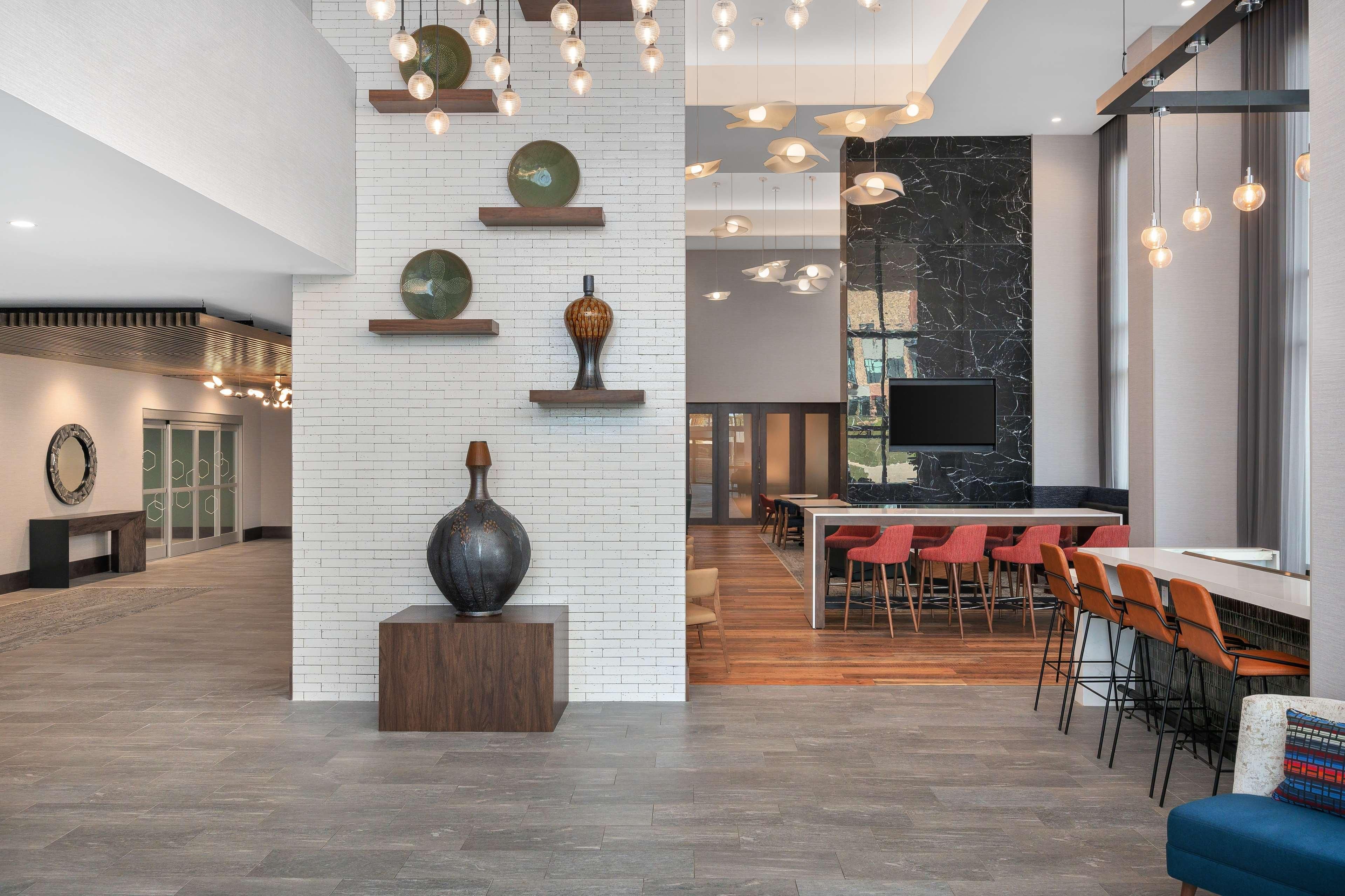 A spacious lobby with a high ceiling, a central staircase, and a modern bar area with red chairs.